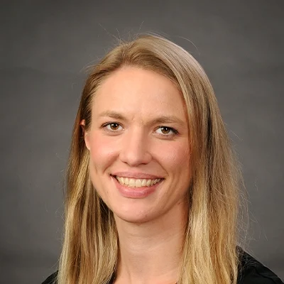 Acupuncturist and Chiropractor Emily Doudlah Smiling In Front Of Grey Background