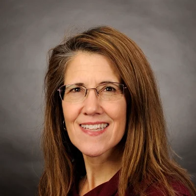 Massage Therapist Laurie Bigelow Smiling In Front Of Grey Background