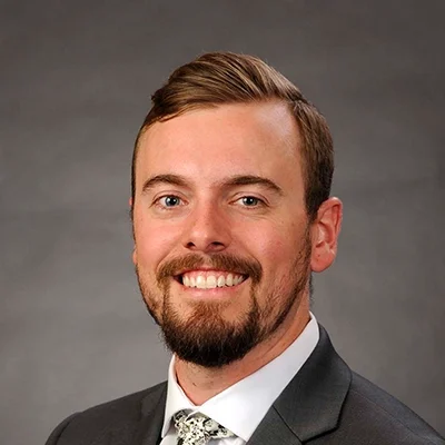 Doctor of Physical Therapy Sam Blum Smiling In Front Of Grey Background