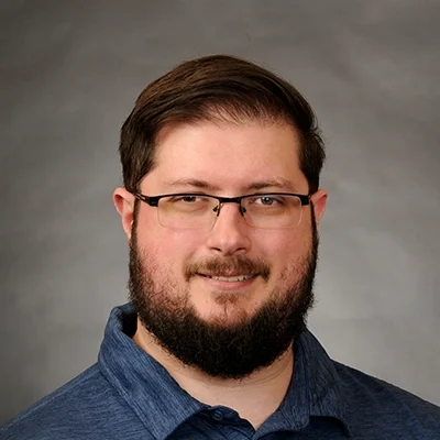 Massage Therapist Alexander Gorski Smiling In Front Of Grey Background
