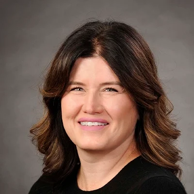 Functional Medicine Nurse Practitioner Kelly Laishes Smiling In Front Of Grey Background
